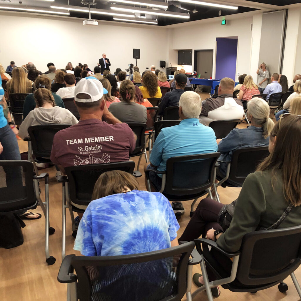 A group of people in a conference room with a presenter at the front of the room speaking.