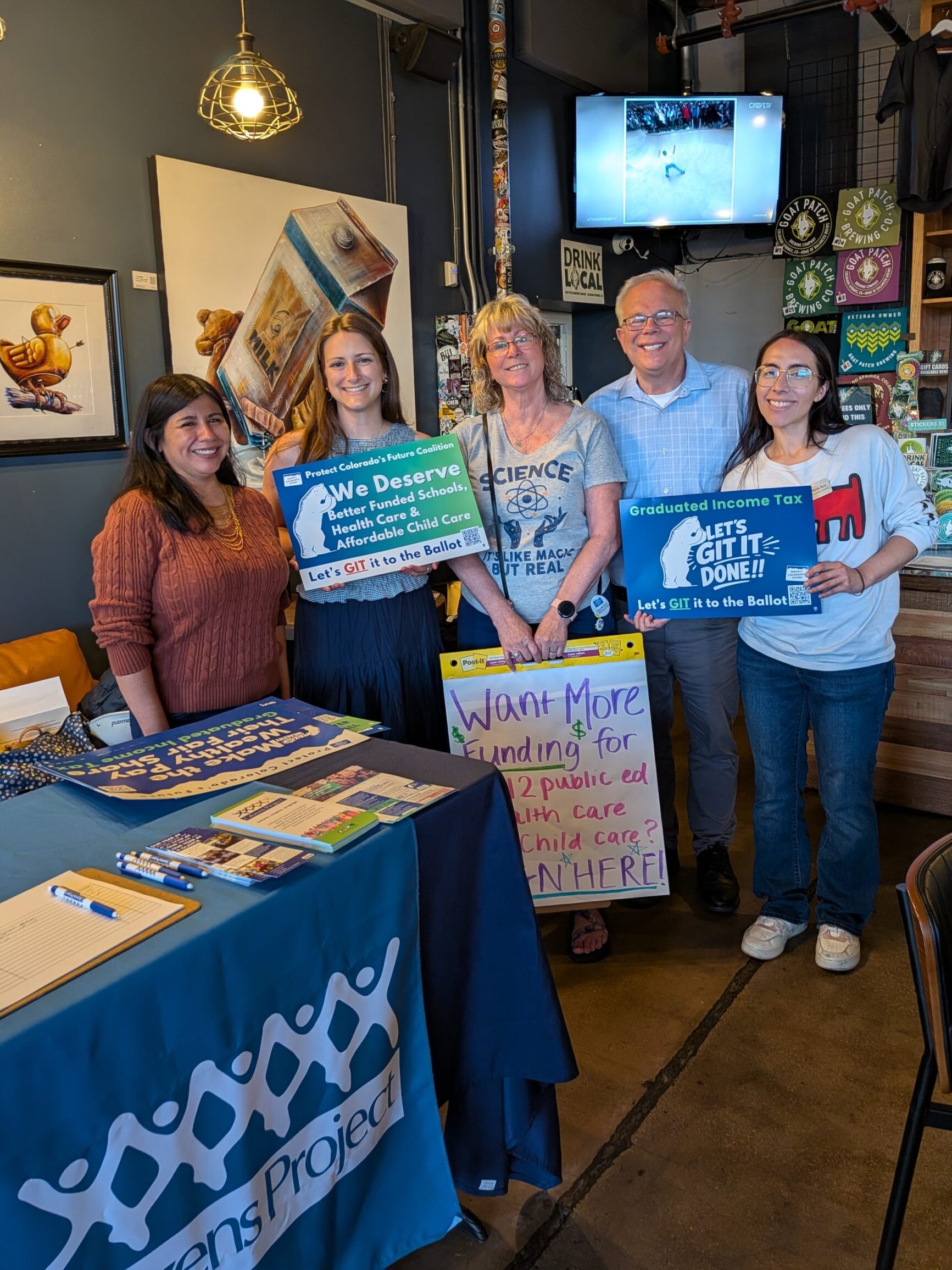 A group of people smiling at the camera and holding signs for the Graduated Income Tax.